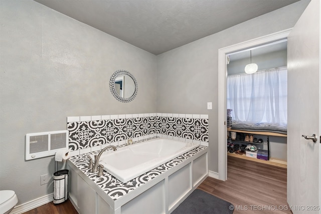 bathroom featuring toilet, baseboards, wood finished floors, and a bath