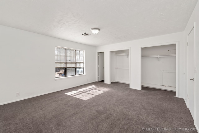 unfurnished bedroom featuring two closets, dark colored carpet, visible vents, a textured ceiling, and baseboards