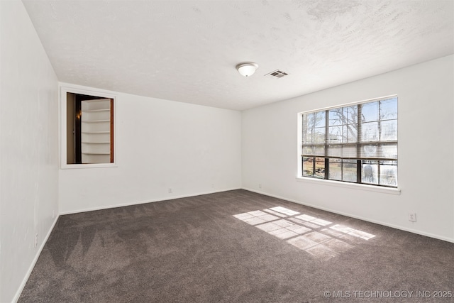 unfurnished room with a textured ceiling, dark carpet, visible vents, and baseboards