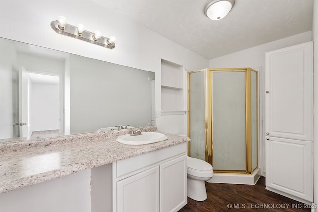 bathroom featuring toilet, a shower stall, wood finished floors, and vanity