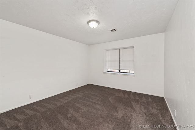 empty room with visible vents, dark carpet, a textured ceiling, and baseboards