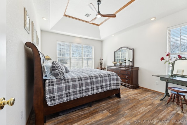 bedroom with a tray ceiling, visible vents, ceiling fan, wood finished floors, and baseboards