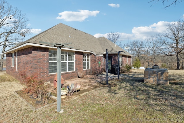 back of property with a patio area, brick siding, a lawn, and roof with shingles