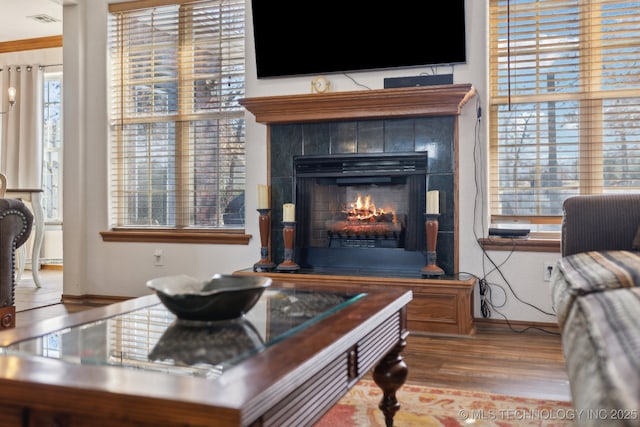 living room with a tile fireplace, visible vents, baseboards, and wood finished floors