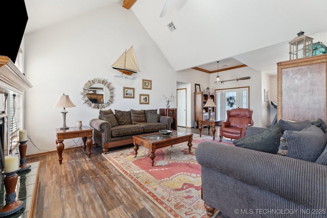 living room with visible vents, a fireplace with raised hearth, a ceiling fan, wood finished floors, and high vaulted ceiling