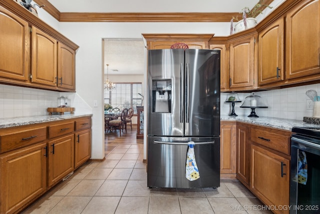 kitchen with light tile patterned floors, stainless steel fridge, brown cabinets, light stone countertops, and black range with electric cooktop