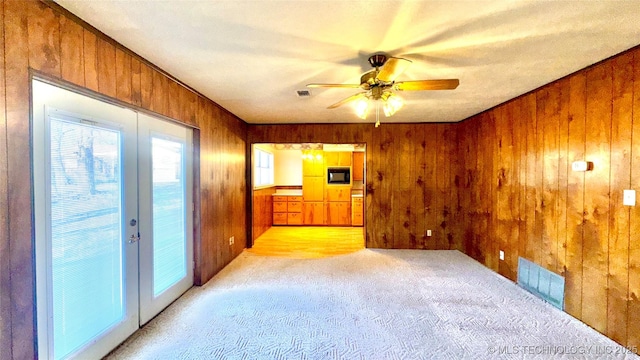 spare room with light colored carpet, french doors, visible vents, and wooden walls