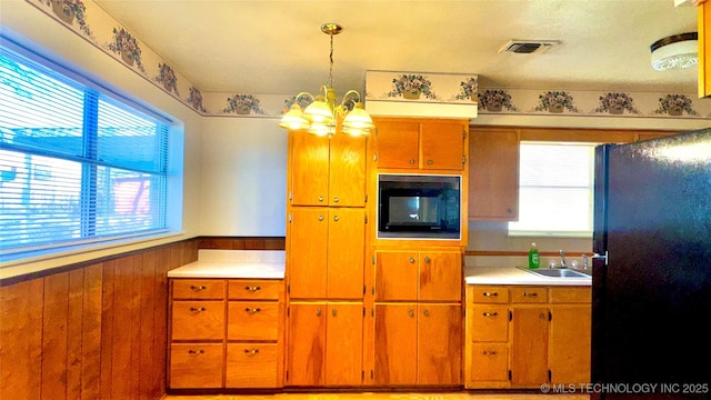 kitchen with light countertops, hanging light fixtures, visible vents, wainscoting, and black appliances