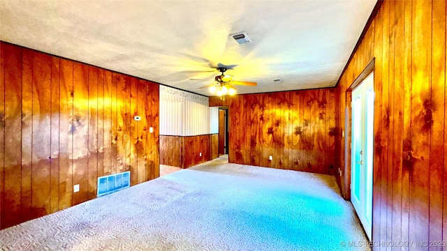 carpeted empty room featuring a ceiling fan, visible vents, and wooden walls