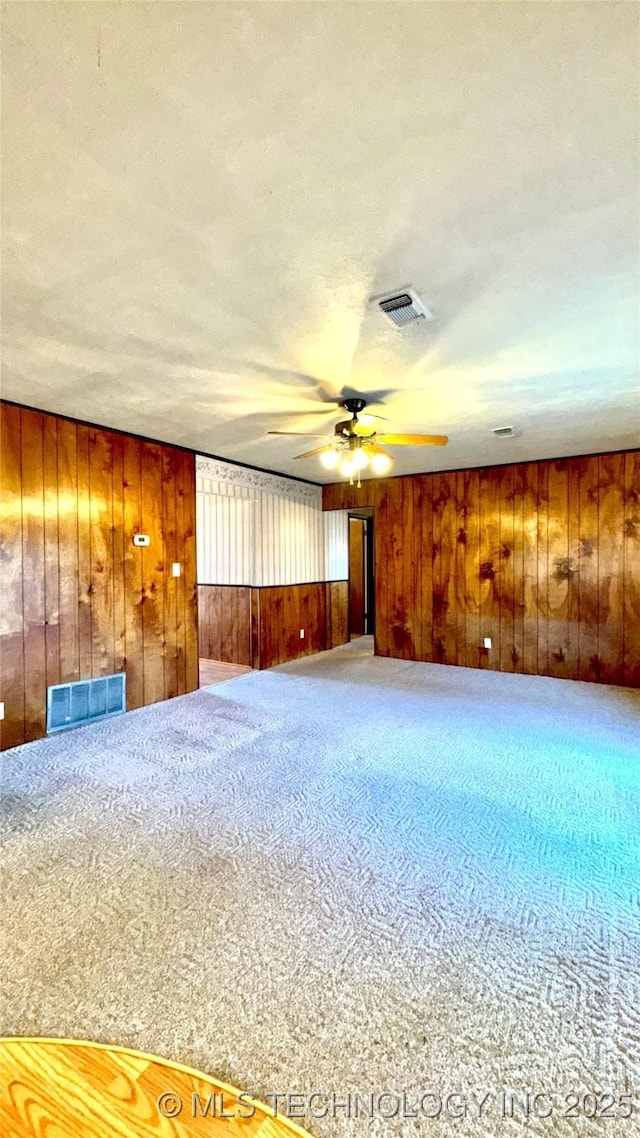 carpeted spare room with wood walls, visible vents, and a ceiling fan