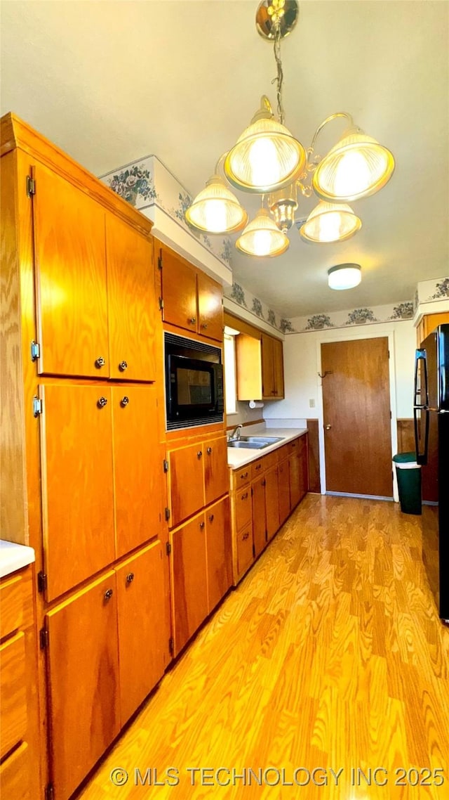 kitchen featuring light wood finished floors, brown cabinetry, light countertops, black appliances, and a sink