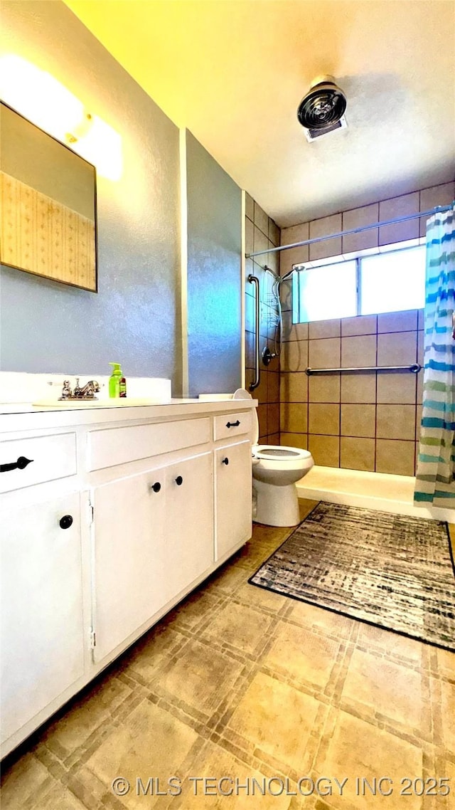 bathroom featuring toilet, tiled shower, and vanity