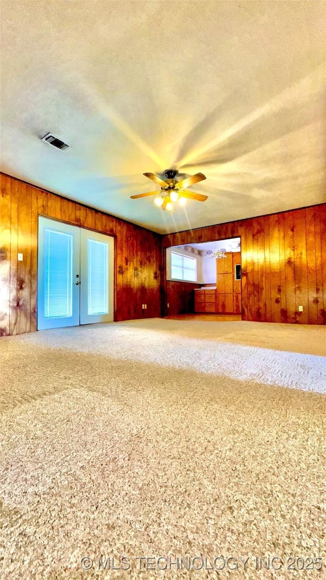 interior space featuring wooden walls, visible vents, ceiling fan, a textured ceiling, and carpet flooring