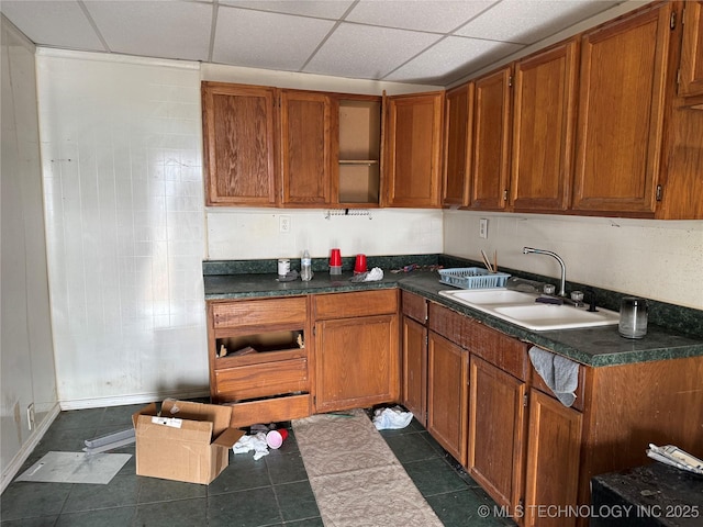 kitchen featuring dark countertops, a paneled ceiling, brown cabinetry, and a sink