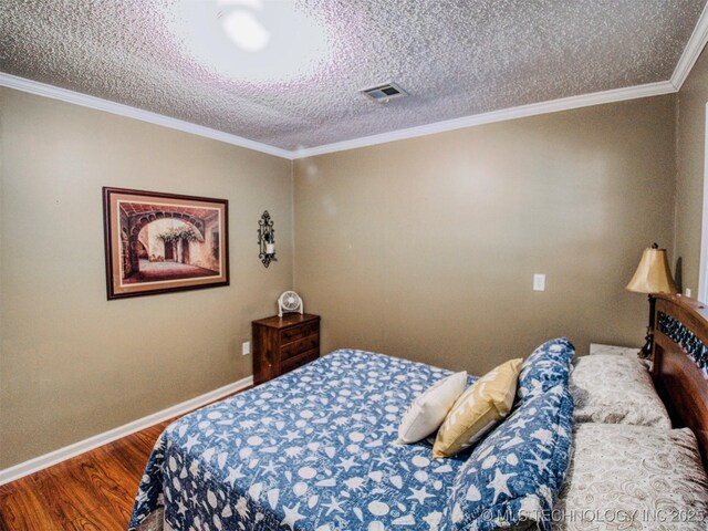 bedroom with a textured ceiling, wood finished floors, visible vents, baseboards, and crown molding