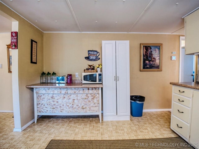 interior space with baseboards, light countertops, white microwave, and white cabinets