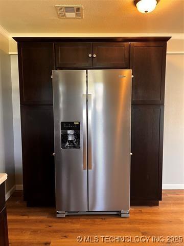 kitchen with stainless steel refrigerator with ice dispenser, light countertops, visible vents, light wood-style floors, and dark brown cabinets