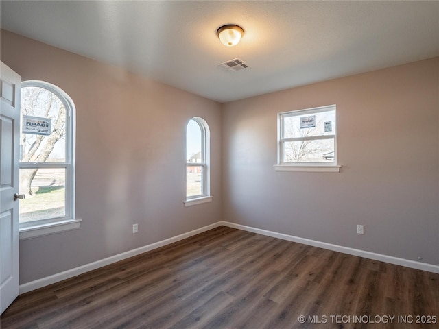 unfurnished room featuring dark wood-style floors, visible vents, and baseboards