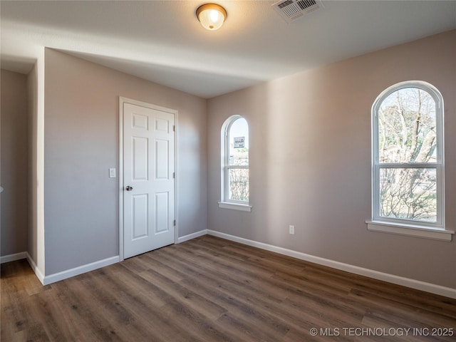 unfurnished room featuring dark wood-style flooring, visible vents, and baseboards