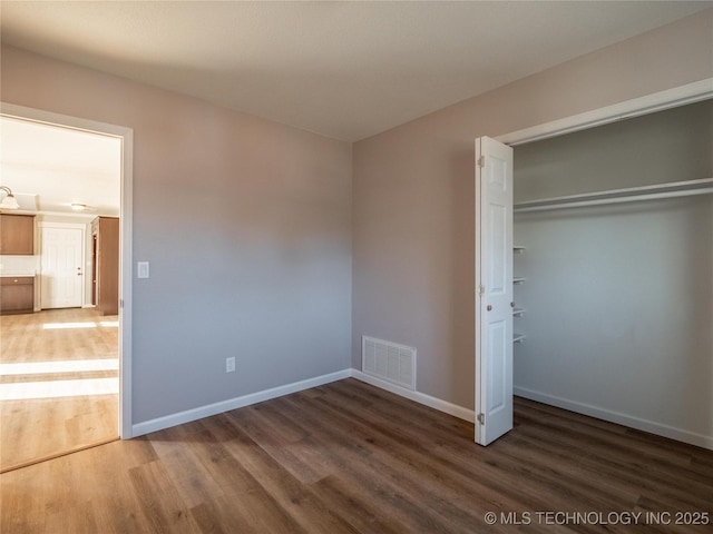 unfurnished bedroom featuring baseboards, a closet, visible vents, and dark wood-type flooring