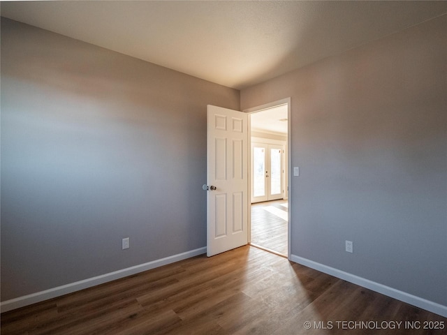 spare room featuring dark wood-style floors, french doors, and baseboards