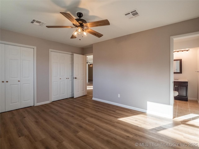 unfurnished bedroom with wood finished floors, visible vents, baseboards, and two closets