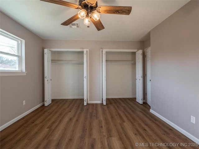 unfurnished bedroom with dark wood-style floors, baseboards, visible vents, and multiple closets