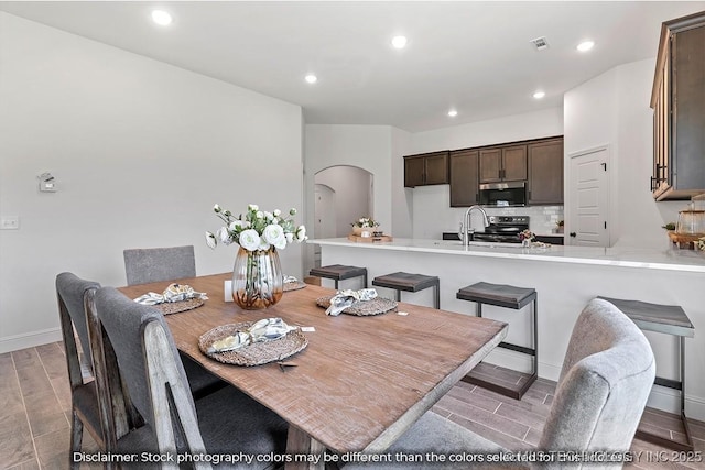 dining area with arched walkways, wood finish floors, visible vents, and recessed lighting