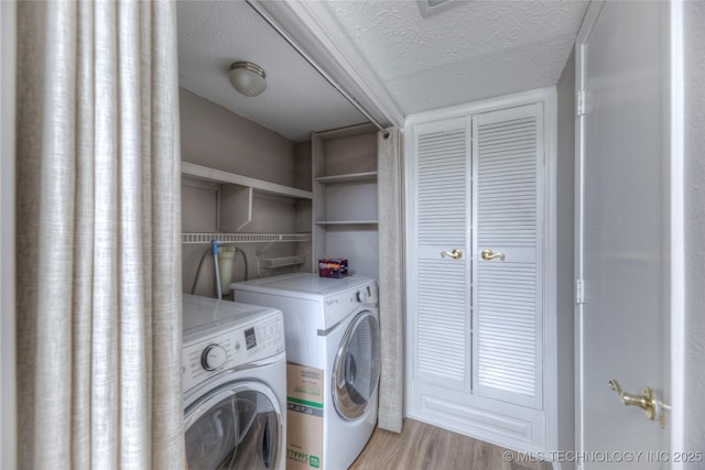 laundry area with a textured ceiling, washing machine and dryer, and light wood-style floors