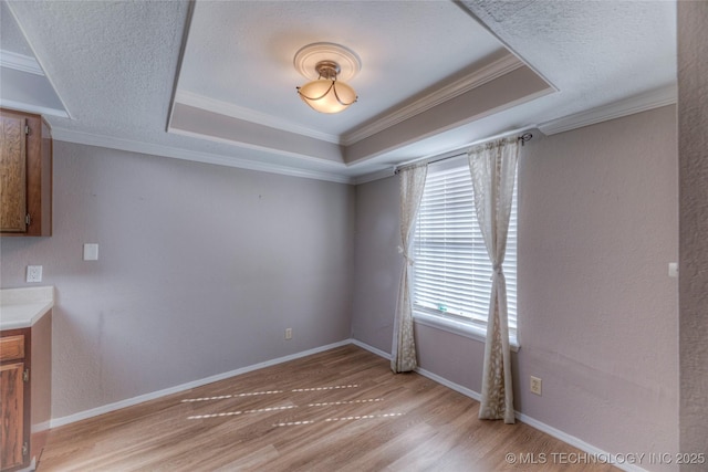 unfurnished room featuring baseboards, a raised ceiling, light wood-style flooring, and crown molding