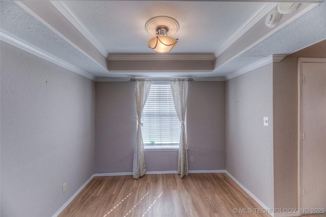 spare room featuring light wood-style flooring, a tray ceiling, a textured ceiling, and ornamental molding