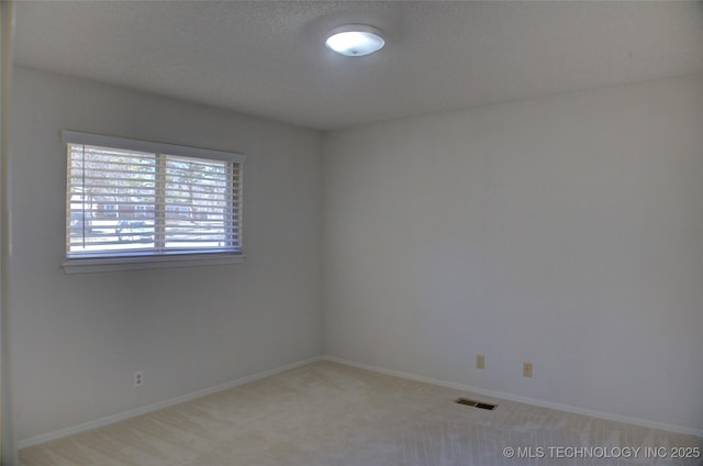 empty room featuring a textured ceiling, light colored carpet, visible vents, and baseboards