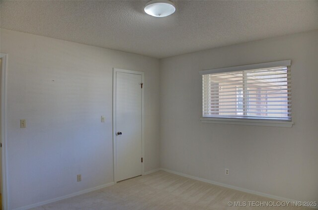 unfurnished room featuring baseboards, a textured ceiling, and light colored carpet