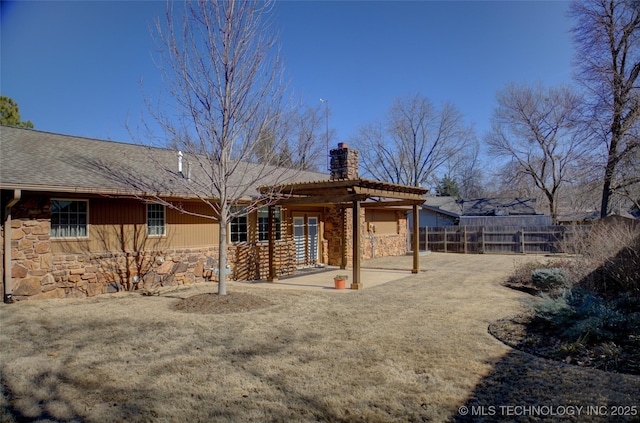 rear view of house featuring a patio, a chimney, fence, a pergola, and stone siding