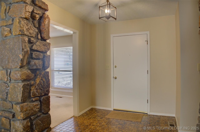 foyer entrance featuring visible vents, baseboards, and a chandelier