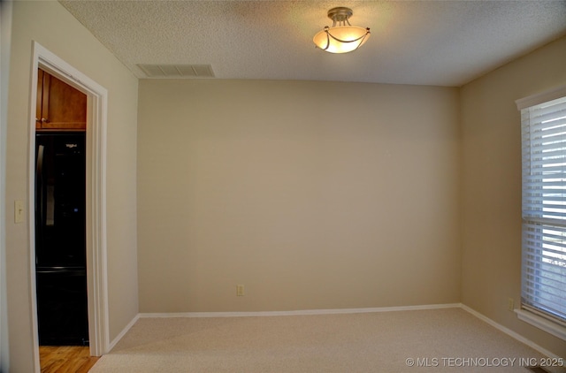 unfurnished room featuring a textured ceiling, light colored carpet, visible vents, and baseboards