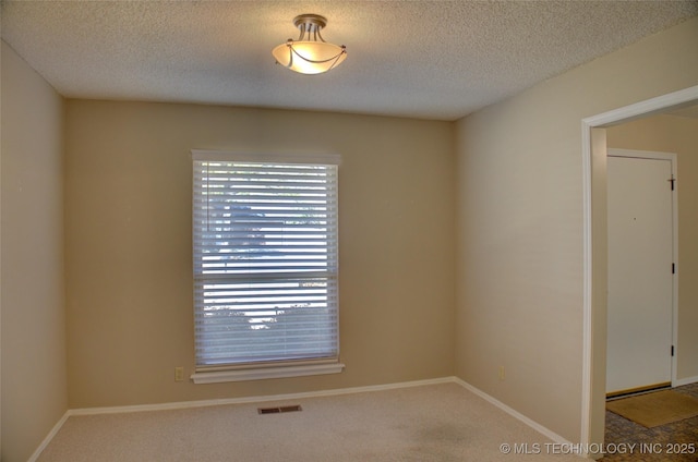 empty room with a textured ceiling, carpet floors, visible vents, and baseboards