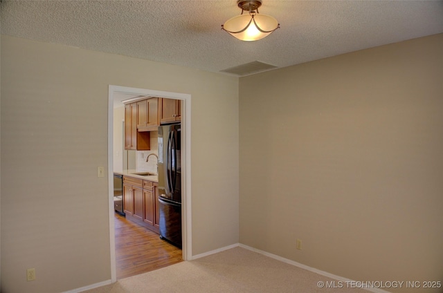 unfurnished room with visible vents, light carpet, a sink, a textured ceiling, and baseboards