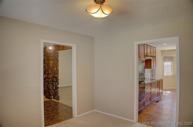 hall with a textured ceiling, light colored carpet, and baseboards