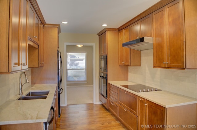 kitchen featuring brown cabinetry, light wood-style floors, a sink, under cabinet range hood, and black appliances