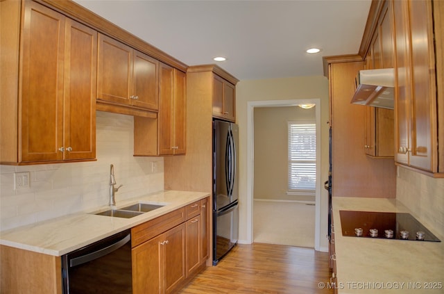 kitchen with black appliances, range hood, brown cabinetry, and a sink