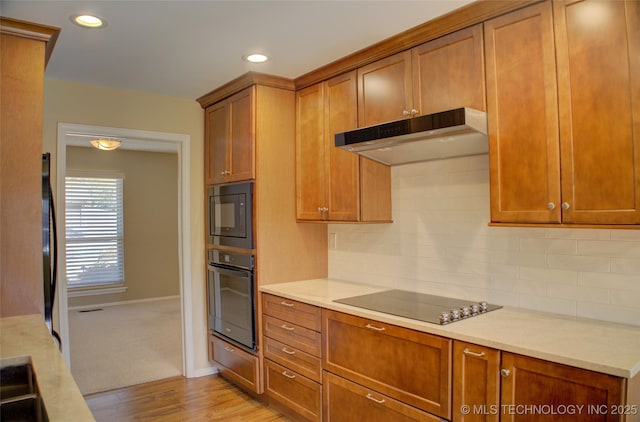 kitchen featuring black appliances, tasteful backsplash, under cabinet range hood, and light countertops