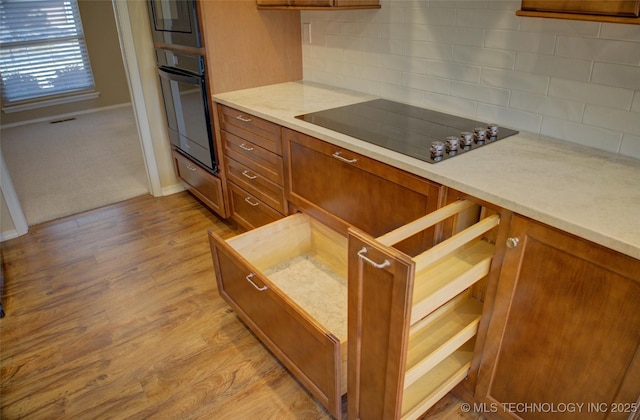 kitchen featuring black appliances, brown cabinetry, light wood finished floors, and light countertops