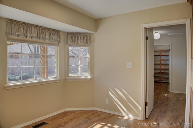 unfurnished room featuring wood finished floors, visible vents, and baseboards