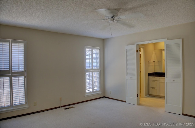 unfurnished bedroom with a textured ceiling, connected bathroom, light colored carpet, visible vents, and baseboards