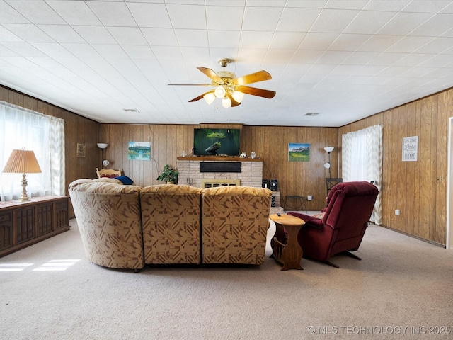 living area with wooden walls, a fireplace, a ceiling fan, and light colored carpet