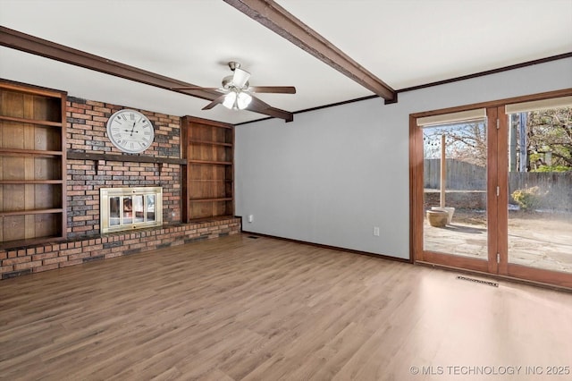 unfurnished living room with built in shelves, a fireplace, wood finished floors, beamed ceiling, and baseboards