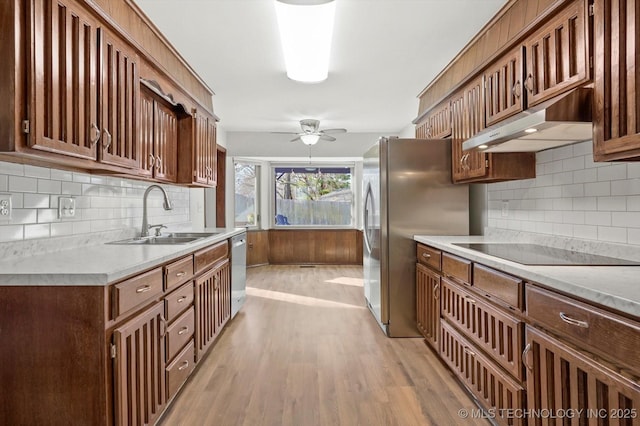 kitchen featuring appliances with stainless steel finishes, light countertops, light wood-type flooring, under cabinet range hood, and a sink