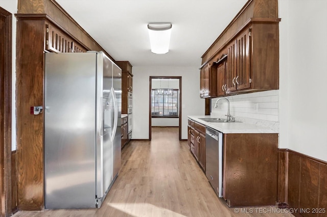 kitchen featuring stainless steel appliances, light countertops, backsplash, a sink, and light wood-type flooring