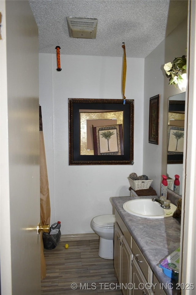 bathroom with toilet, vanity, a textured ceiling, and wood finished floors